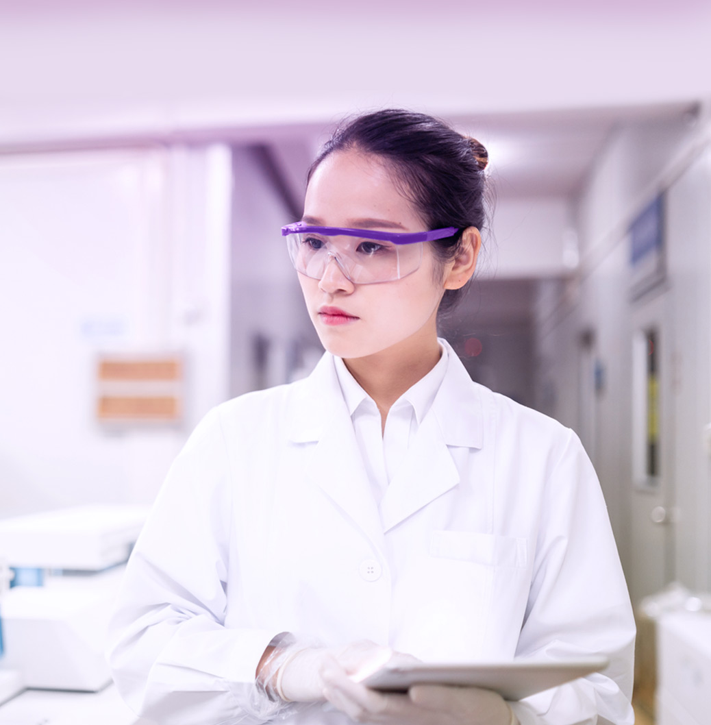 Uma senhora devidamente equipada para o trabalho em laboratório, observa algo enquanto segura o seu tablet
