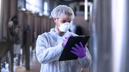 Profissional de laboratório devidamente equipado, tira notas durante uma visita a um laboratório.