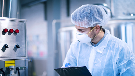 Profissional de laboratório devidamente equipado, tira notas durante a monitorização de equipamento numa visita a um laboratório