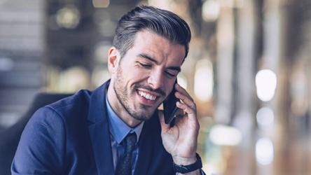 Um homem sorridente, de fato, participa numa chamada telefónica usando um telemóvel.